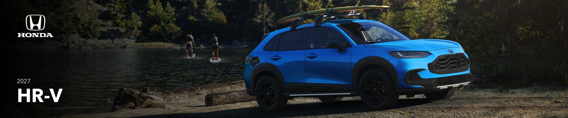 An exterior shot of a blue 2027 Honda HR-V with a surfboard o its roof rack parked on a forested waterfront.