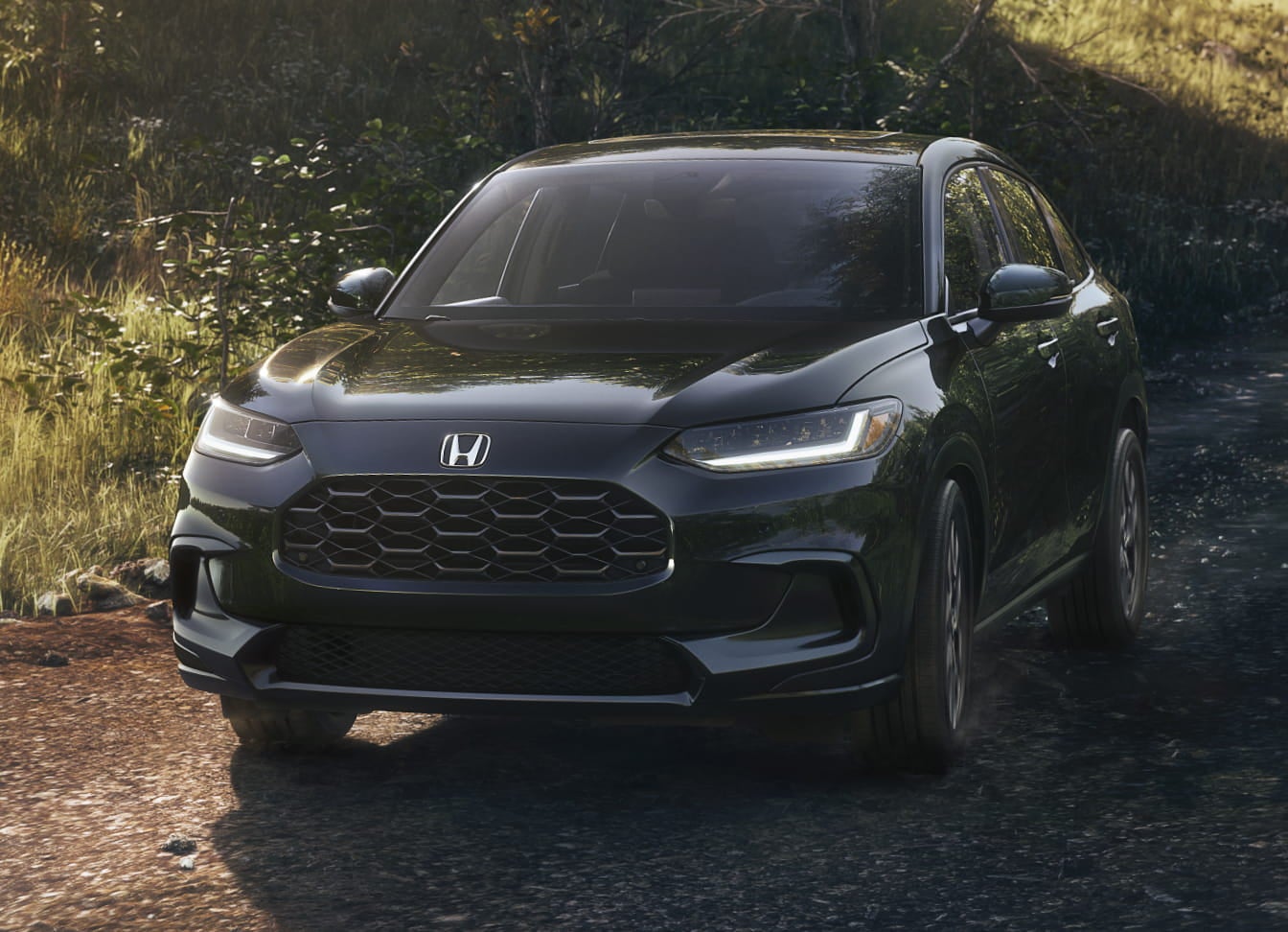A sleek black HR-V SUV drives along a forested path, sunlight glinting off its polished surface.