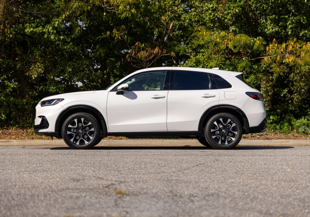 Driver's side view of a 2025 Honda HR-V parked on a paved road in front of a wooded area